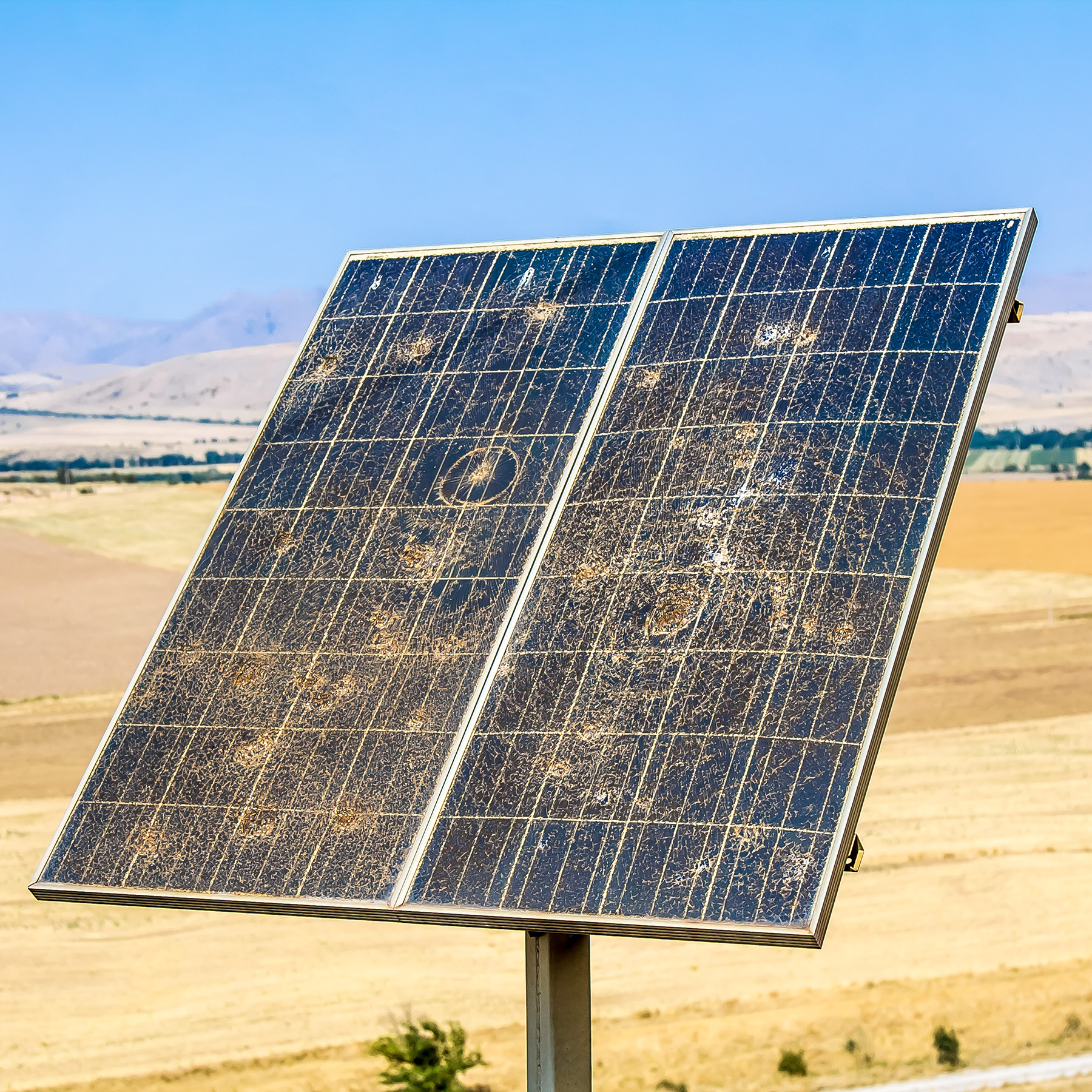 An array of solar panels, damaged by sand, wind, and other objects.